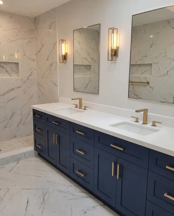 Navy double vanity with a quartz top, brass fixtures and bookmatched marble-look slab walls
